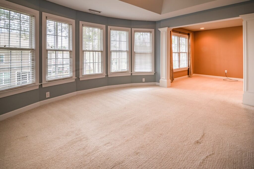 pexels-photo-3990587 An empty, spacious room with large windows and carpet flooring, ideal for various uses.