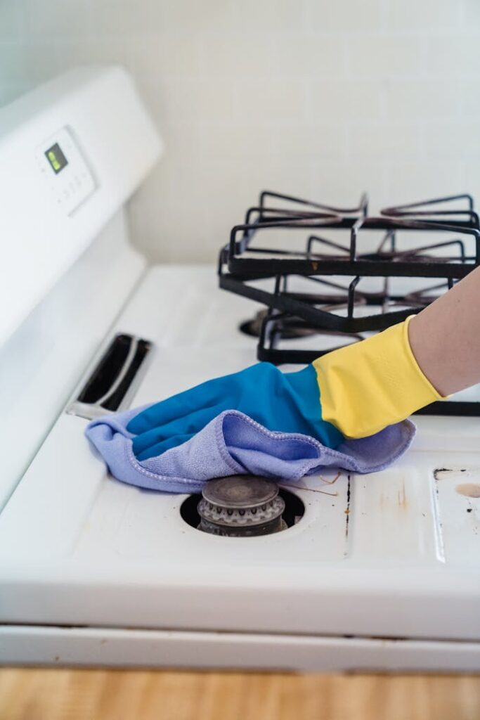 pexels-photo-9462301 A close-up of a hand in gloves cleaning a gas stove with a cloth.